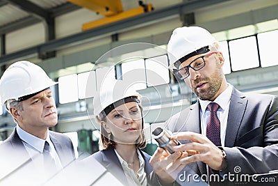 Mid adult businessman explaining machine part of colleagues in metal industry Stock Photo