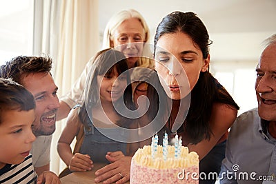 Mid adult white woman blowing out candles on birthday cake watched by her family, close up Stock Photo