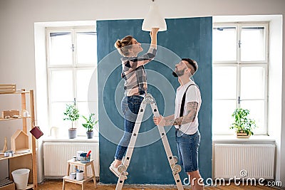 Mid adults couple changing light bulb indoors at home, relocation and diy concept. Stock Photo