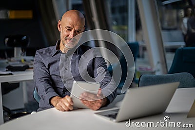 Mid aged professional man sitting at the office and using touchpad and notebook for work Stock Photo