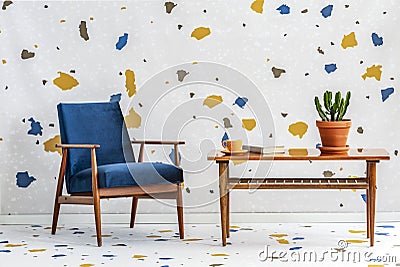 Mid-century modern, navy blue armchair and a retro wooden table in a white living room interior with lastrico pattern on the wall Stock Photo