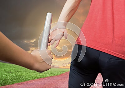 Mid-section of athlete passing the baton to teammate in stadium at sunset Stock Photo