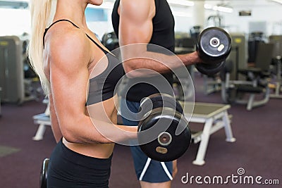 Mid section of couple exercising with dumbbells in gym Stock Photo