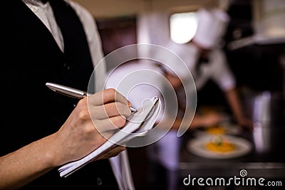 Female waitress noting an order on notepad in kitchen Stock Photo