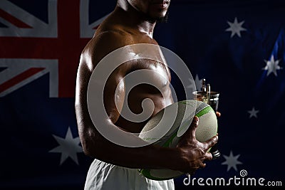 Mid section of shirtless man with trophy and rugby ball against Australian flag Stock Photo