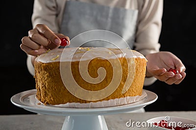 Woman toping a fresh baked cake with cherry Stock Photo