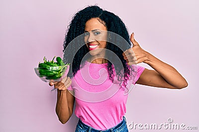 Middle age african american woman holding green pepper smiling happy and positive, thumb up doing excellent and approval sign Stock Photo