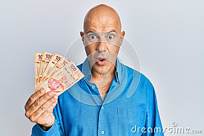 Middle age bald man holding mexican pesos scared and amazed with open mouth for surprise, disbelief face Stock Photo