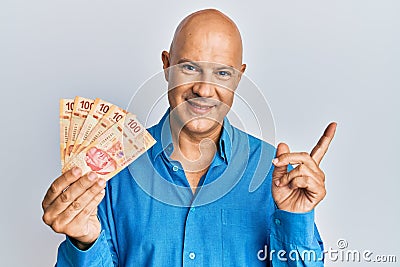 Middle age bald man holding mexican pesos smiling happy pointing with hand and finger to the side Stock Photo