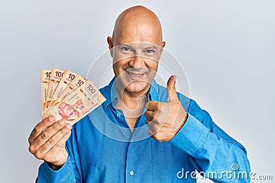 Middle age bald man holding mexican pesos smiling happy and positive, thumb up doing excellent and approval sign Stock Photo