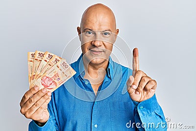 Middle age bald man holding mexican pesos smiling with an idea or question pointing finger with happy face, number one Stock Photo