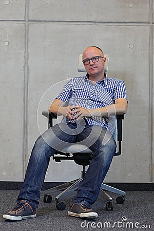 Middle age balding man with eyeglasses bad sitting position on chair in office Stock Photo