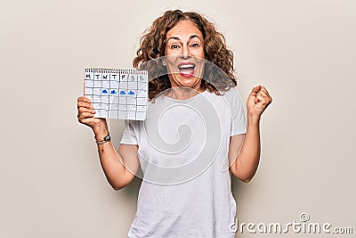 Middle age beautiful woman holding climatology calendar showing cloudy and rainy weather screaming proud, celebrating victory and Stock Photo