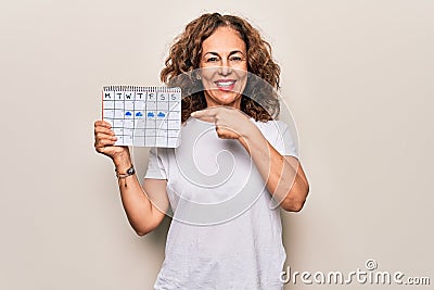 Middle age beautiful woman holding climatology calendar showing cloudy and rainy weather smiling happy pointing with hand and Stock Photo