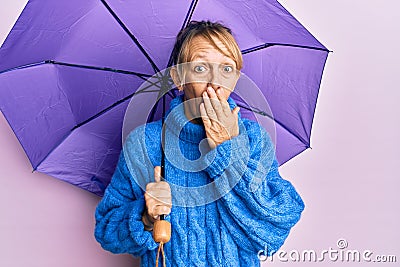 Middle age blonde woman holding purple umbrella covering mouth with hand, shocked and afraid for mistake Stock Photo