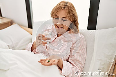 Middle age blonde woman illness taking pill lying on the bed at home Stock Photo