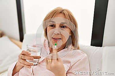 Middle age blonde woman illness taking pill lying on the bed at home Stock Photo