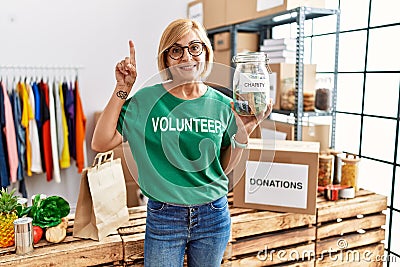 Middle age blonde woman wearing volunteer t shirt holding charity money surprised with an idea or question pointing finger with Stock Photo