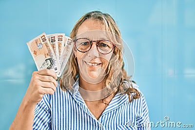 Middle age caucasian woman smiling happy holding uk pounds banknotes standing at the city Editorial Stock Photo