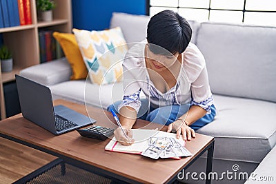 Middle age chinese woman writing on notebook accounting at home Stock Photo