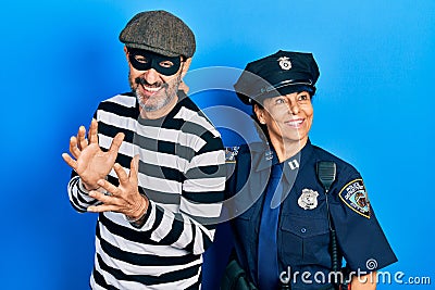 Middle age couple of hispanic woman and man wearing thief and police uniform smiling looking to the side and staring away thinking Stock Photo