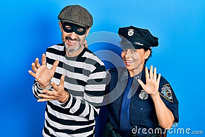 Middle age couple of hispanic woman and man wearing thief and police uniform waiving saying hello happy and smiling, friendly Stock Photo