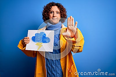Middle age curly hair woman wearing rain coat holding banner with cloud and thunder with open hand doing stop sign with serious Stock Photo