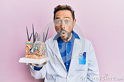 Middle age doctor man holding model of human anatomical skin and hair scared and amazed with open mouth for surprise, disbelief Stock Photo