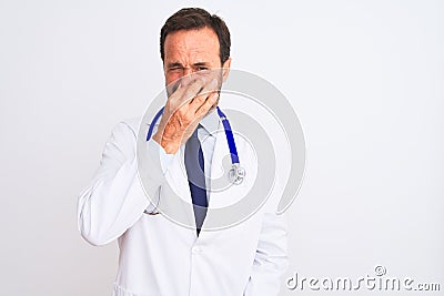 Middle age doctor man wearing coat and stethoscope standing over isolated white background smelling something stinky and Stock Photo