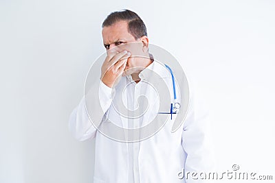 Middle age doctor man wearing stethoscope and medical coat over white background smelling something stinky and disgusting, Stock Photo