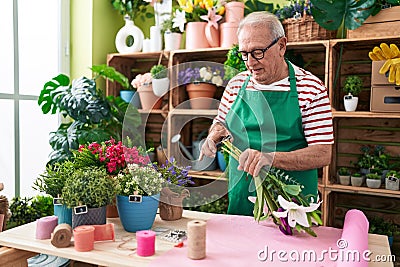 Middle age grey-haired man florist cutting stem at flower shop Stock Photo