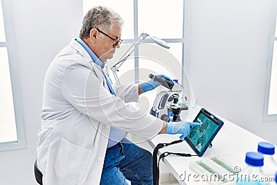 Middle age grey-haired man wearing scientist uniform looking embryology image touchpad at laboratory Stock Photo