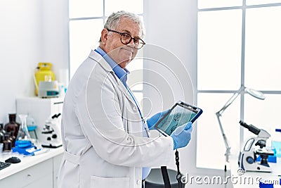 Middle age grey-haired man wearing scientist uniform looking embryology image touchpad at laboratory Stock Photo