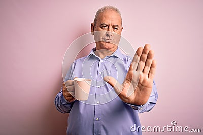 Middle age handsome hoary man drinking mug of coffee over isolated pink background with open hand doing stop sign with serious and Stock Photo
