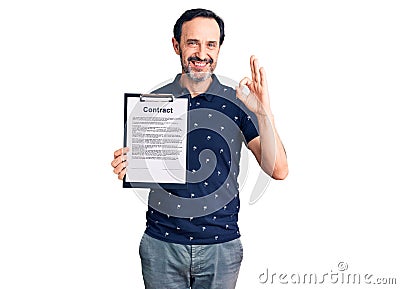 Middle age handsome man holding clipboard with contract document doing ok sign with fingers, smiling friendly gesturing excellent Stock Photo