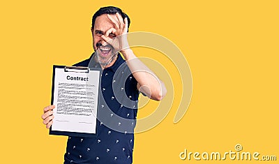 Middle age handsome man holding clipboard with contract document smiling happy doing ok sign with hand on eye looking through Stock Photo