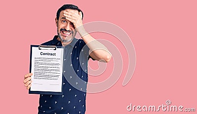 Middle age handsome man holding clipboard with contract document stressed and frustrated with hand on head, surprised and angry Stock Photo