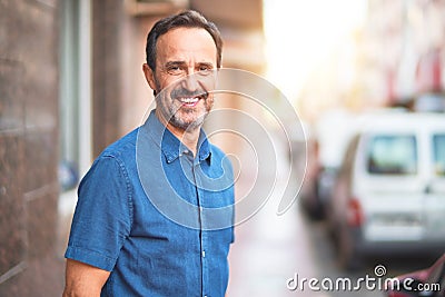 Middle age handsome man standing on the street smiling Stock Photo