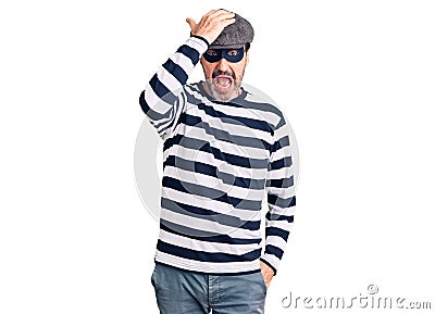 Middle age handsome man wearing burglar mask surprised with hand on head for mistake, remember error Stock Photo