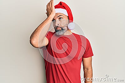 Middle age handsome man wearing christmas hat and summer t-shirt surprised with hand on head for mistake, remember error Stock Photo