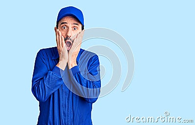 Middle age handsome man wearing mechanic uniform afraid and shocked, surprise and amazed expression with hands on face Stock Photo