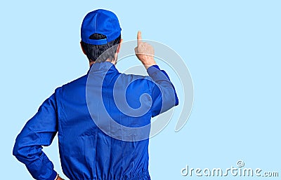 Middle age handsome man wearing mechanic uniform posing backwards pointing ahead with finger hand Stock Photo