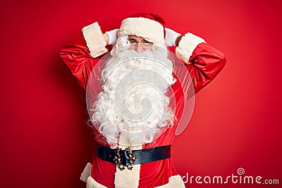Middle age handsome man wearing Santa costume standing over isolated red background relaxing and stretching, arms and hands behind Stock Photo