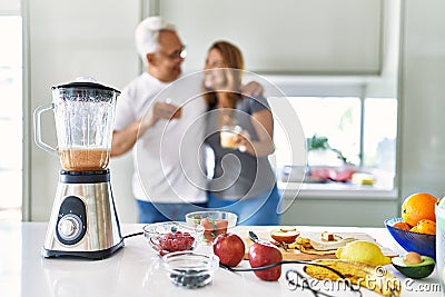 Middle age hispanic couple smiling happy and hugging drinking glass of smoothie at the kitchen Stock Photo