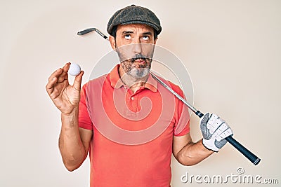 Middle age hispanic man holding golf club and ball making fish face with mouth and squinting eyes, crazy and comical Stock Photo