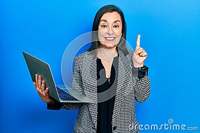 Middle age hispanic woman holding laptop smiling with an idea or question pointing finger with happy face, number one Editorial Stock Photo
