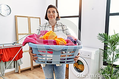 Middle age hispanic woman holding laundry basket smiling looking to the side and staring away thinking Stock Photo