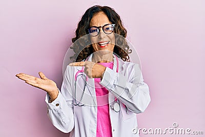 Middle age hispanic woman wearing doctor uniform and glasses amazed and smiling to the camera while presenting with hand and Stock Photo