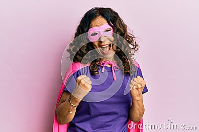 Middle age hispanic woman wearing super hero costume celebrating surprised and amazed for success with arms raised and eyes closed Stock Photo