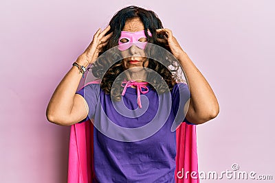 Middle age hispanic woman wearing super hero costume with hand on head, headache because stress Stock Photo